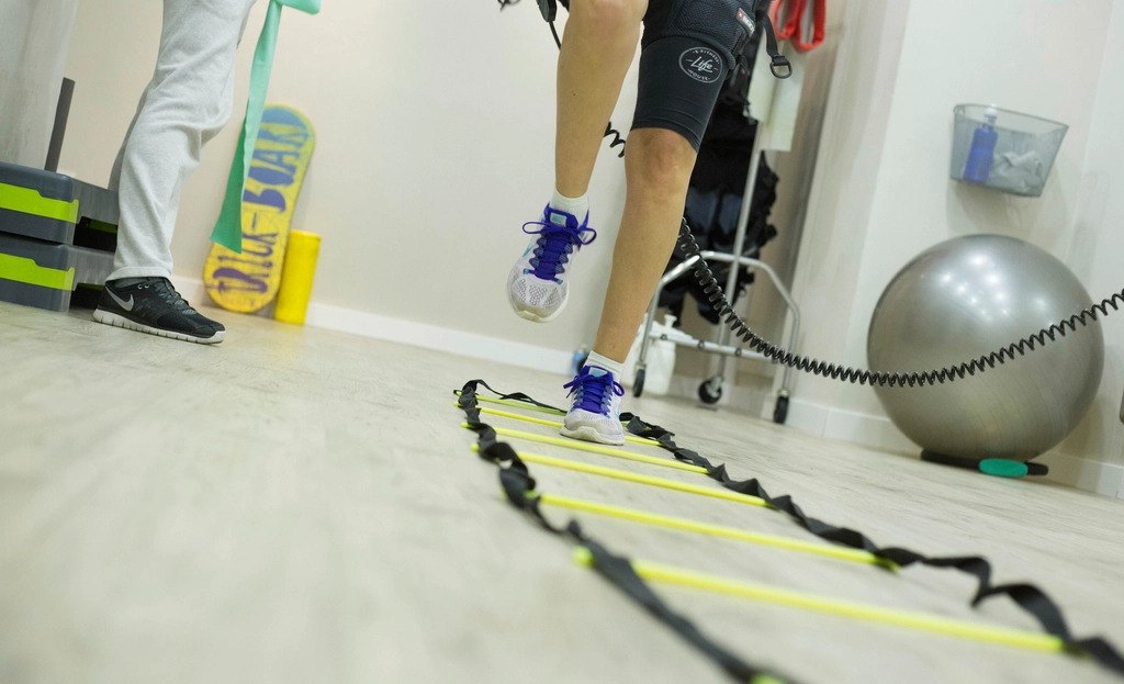 Pacient trénuje koordinaci na žebříku v rehabilitačním sále, vedle terapeut